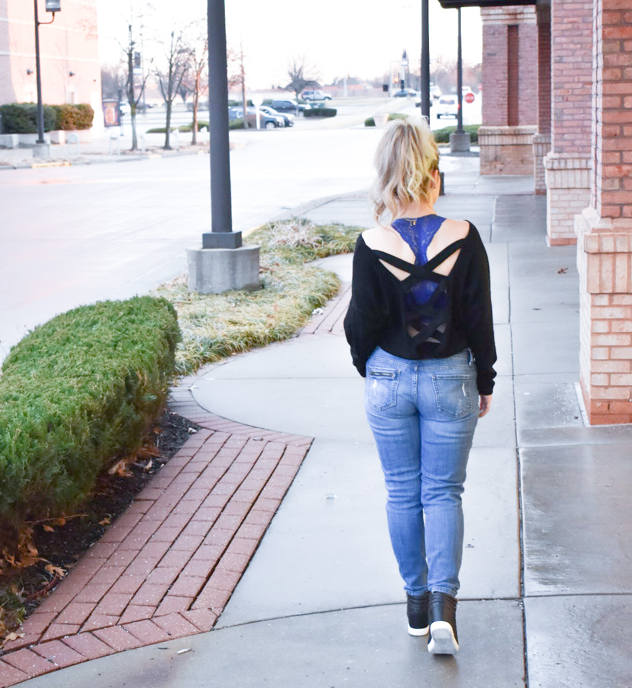 Black Criss-Cross Sweater + Bralette for Large Bust: This black criss-cross sweater styled with ripped jeans and black wedge sneakers is the perfect mix of sporty and sexy for your next date night! Plus, the perfect affordable bralette for large bust ladies. Fashion blogger COVET by tricia shows how to style a perfect date night look mixing black and denim.