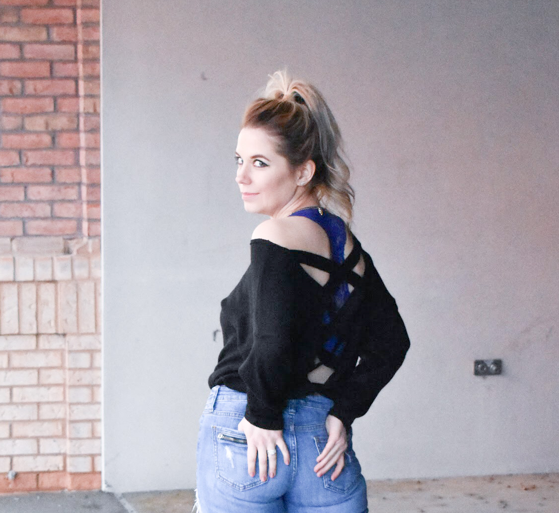 Black Criss-Cross Sweater + Bralette for Large Bust: This black criss-cross sweater styled with ripped jeans and black wedge sneakers is the perfect mix of sporty and sexy for your next date night! Plus, the perfect affordable bralette for large bust ladies. Fashion blogger COVET by tricia shows how to style a perfect date night look mixing black and denim.