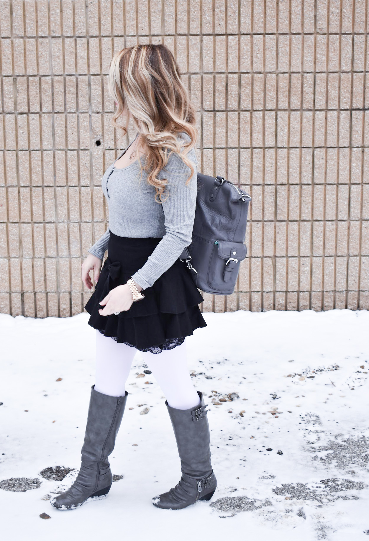 Fashion blogger COVET by tricia styles a ruffled black mini skirt with white tights, a grey bodysuit, grey wedge boots ,and a gorgeous Lily Jade diaper bag. This black mini skirt with ruffles is an affordable statement piece for your wardrobe. Check out this cute winter date night look from Kansas City fashion blogger COVET by tricia.