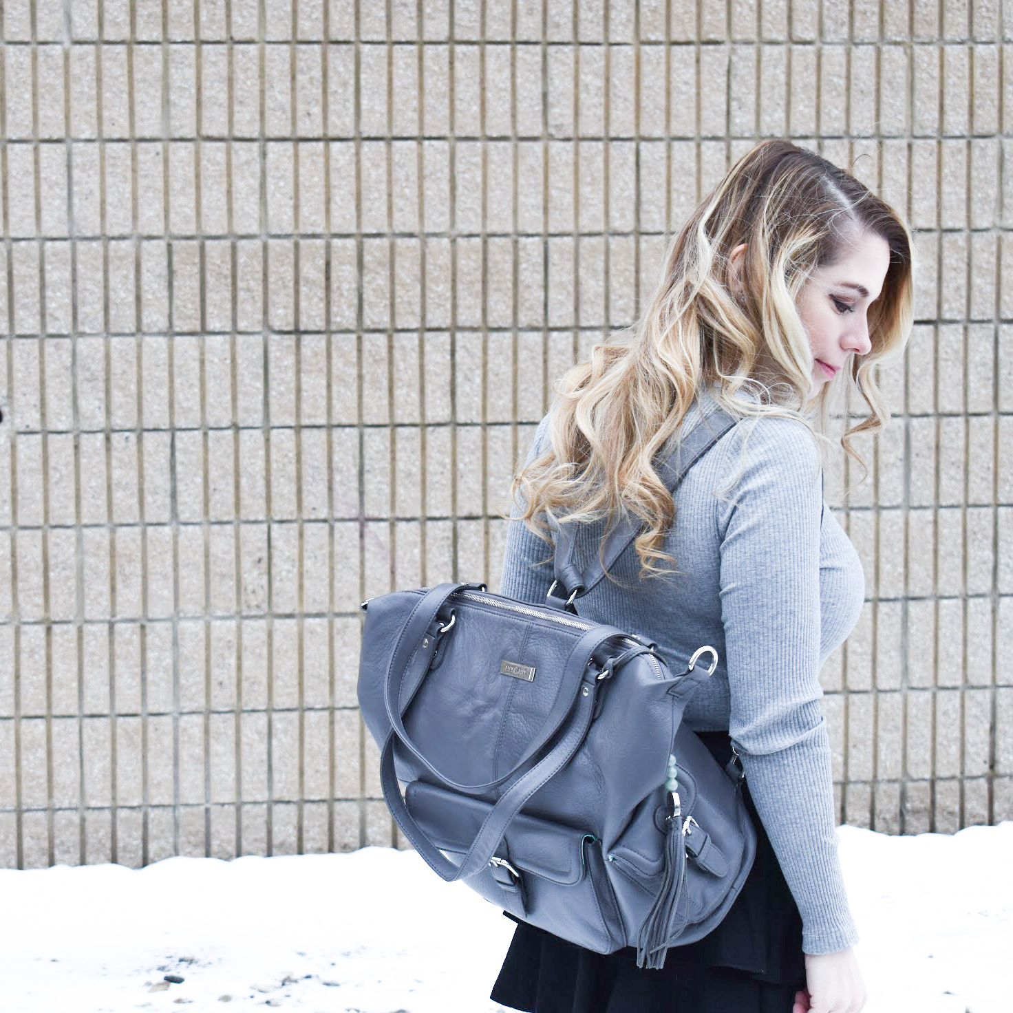 Fashion blogger COVET by tricia styles a ruffled black mini skirt with white tights, a grey bodysuit, grey wedge boots ,and a gorgeous Lily Jade diaper bag. This black mini skirt with ruffles is an affordable statement piece for your wardrobe. Check out this cute winter date night look from Kansas City fashion blogger COVET by tricia.