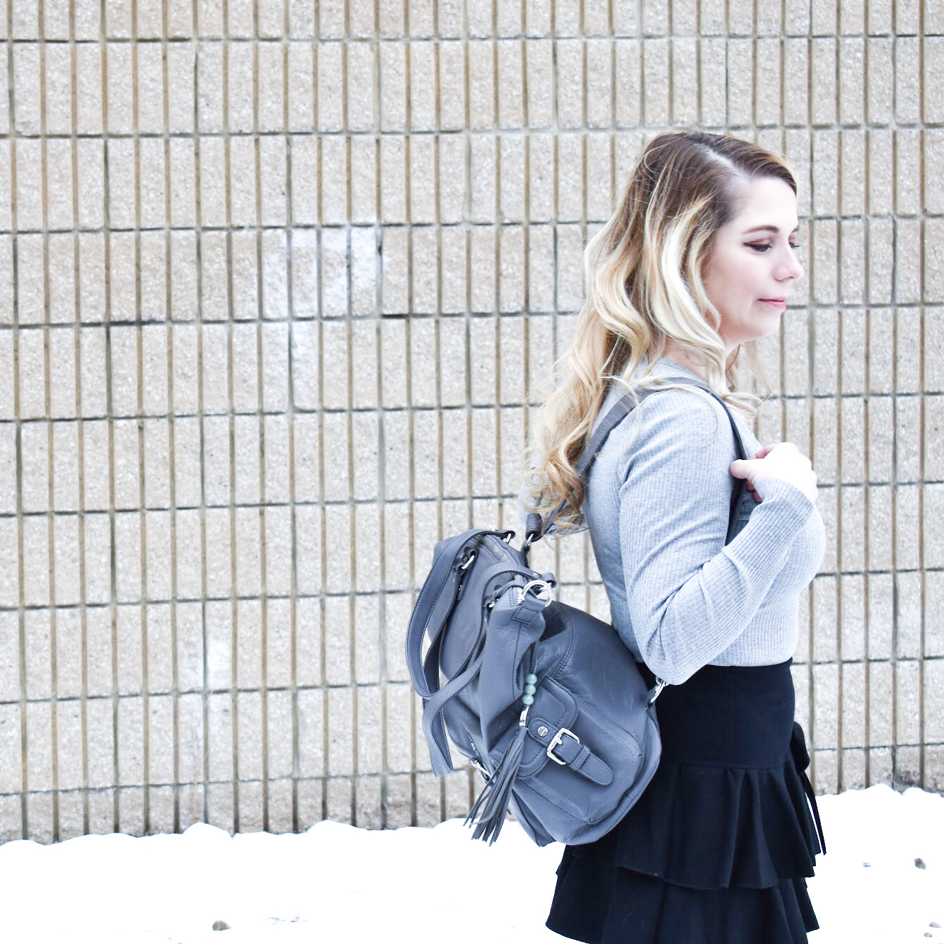 Fashion blogger COVET by tricia styles a ruffled black mini skirt with white tights, a grey bodysuit, grey wedge boots ,and a gorgeous Lily Jade diaper bag. This black mini skirt with ruffles is an affordable statement piece for your wardrobe. Check out this cute winter date night look from Kansas City fashion blogger COVET by tricia.