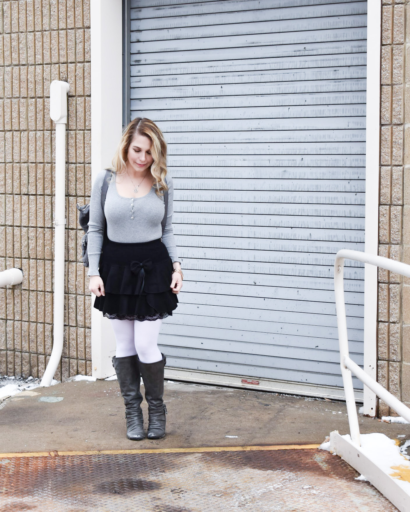 Fashion blogger COVET by tricia styles a ruffled black mini skirt with white tights, a grey bodysuit, grey wedge boots ,and a gorgeous Lily Jade diaper bag. This black mini skirt with ruffles is an affordable statement piece for your wardrobe. Check out this cute winter date night look from Kansas City fashion blogger COVET by tricia.