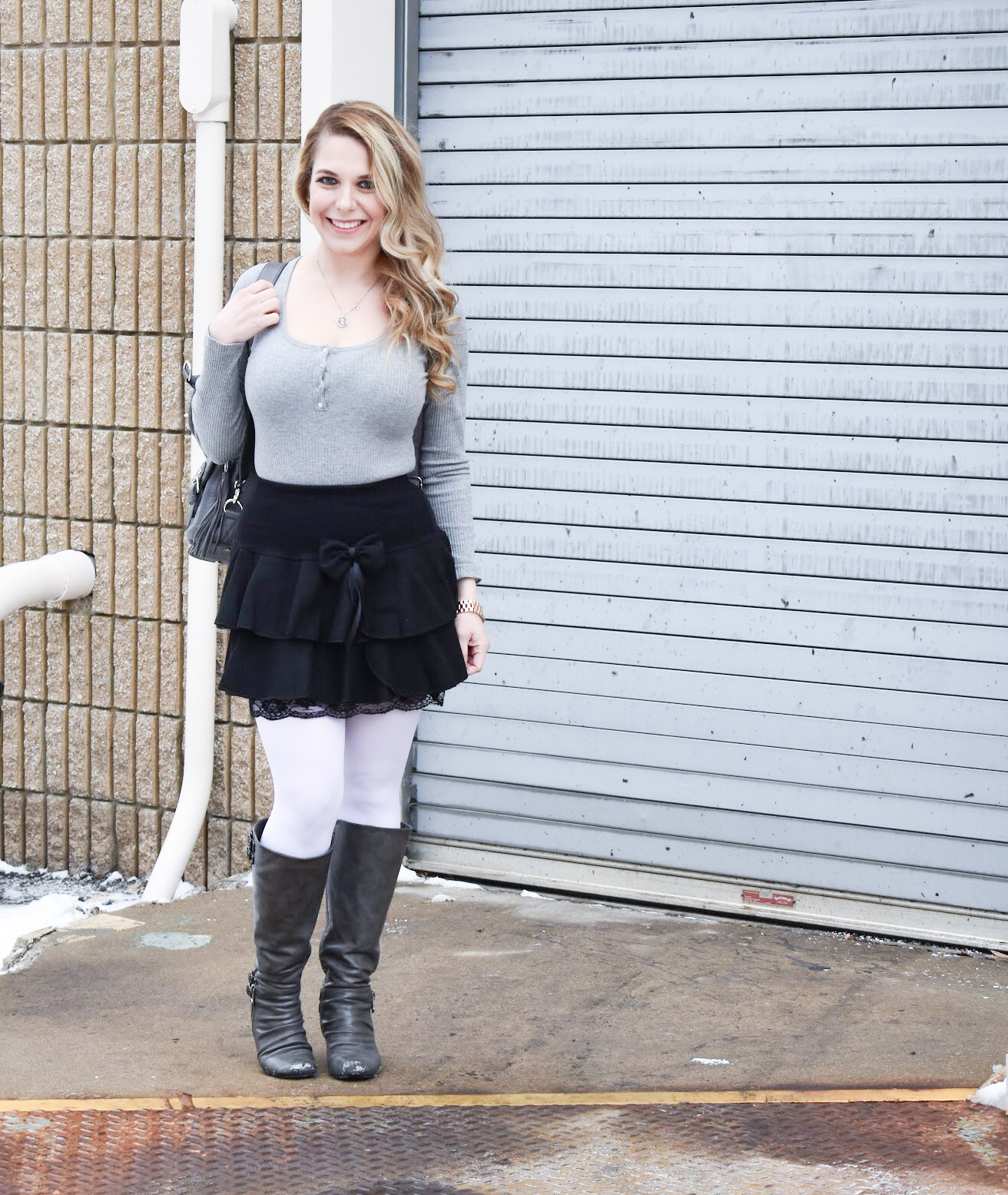 Fashion blogger COVET by tricia styles a ruffled black mini skirt with white tights, a grey bodysuit, grey wedge boots ,and a gorgeous Lily Jade diaper bag. This black mini skirt with ruffles is an affordable statement piece for your wardrobe. Check out this cute winter date night look from Kansas City fashion blogger COVET by tricia.