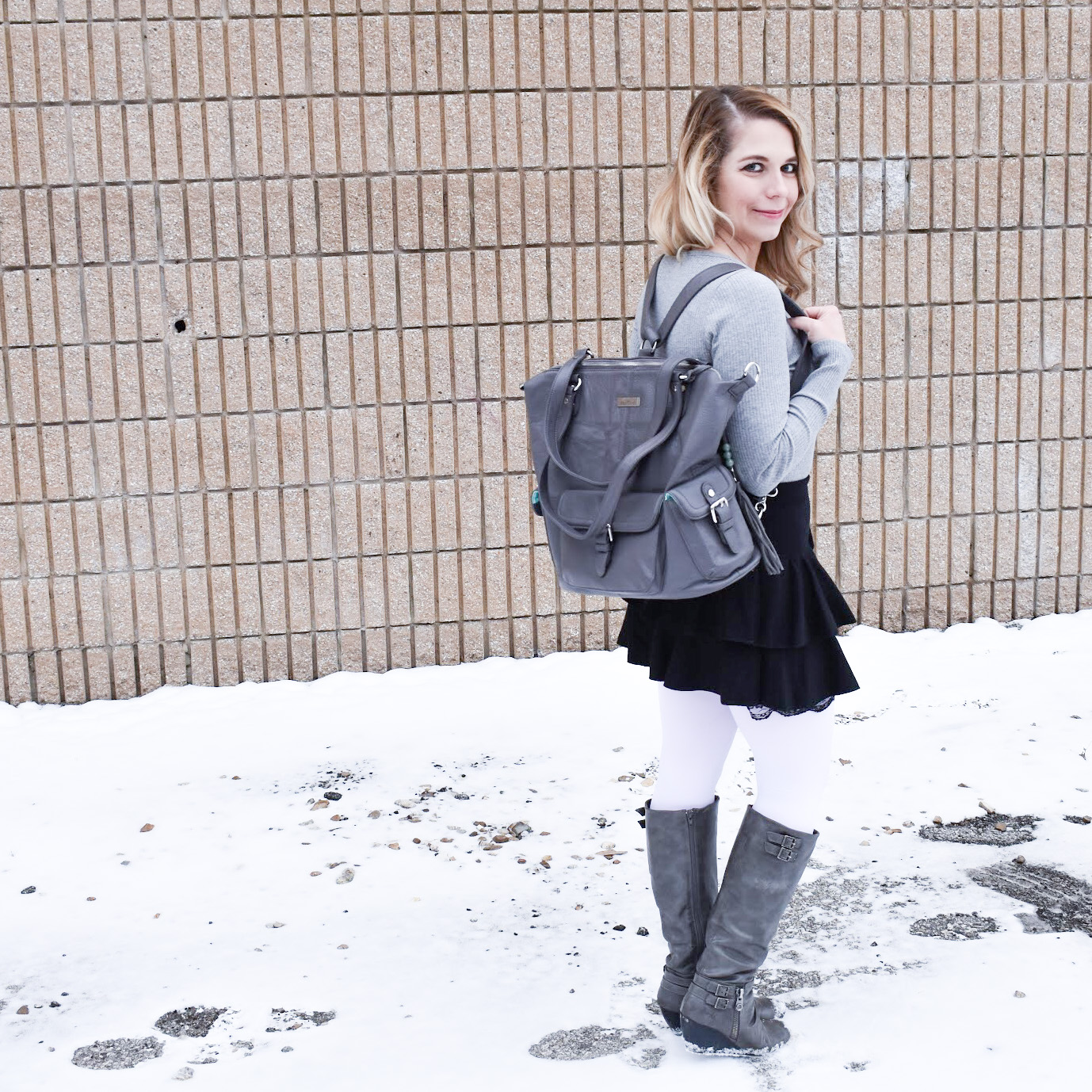 Fashion blogger COVET by tricia styles a ruffled black mini skirt with white tights, a grey bodysuit, grey wedge boots ,and a gorgeous Lily Jade diaper bag. This black mini skirt with ruffles is an affordable statement piece for your wardrobe. Check out this cute winter date night look from Kansas City fashion blogger COVET by tricia.