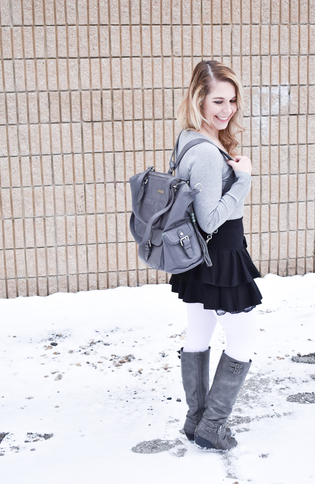 Fashion blogger COVET by tricia styles a ruffled black mini skirt with white tights, a grey bodysuit, grey wedge boots ,and a gorgeous Lily Jade diaper bag. This black mini skirt with ruffles is an affordable statement piece for your wardrobe. Check out this cute winter date night look from Kansas City fashion blogger COVET by tricia.