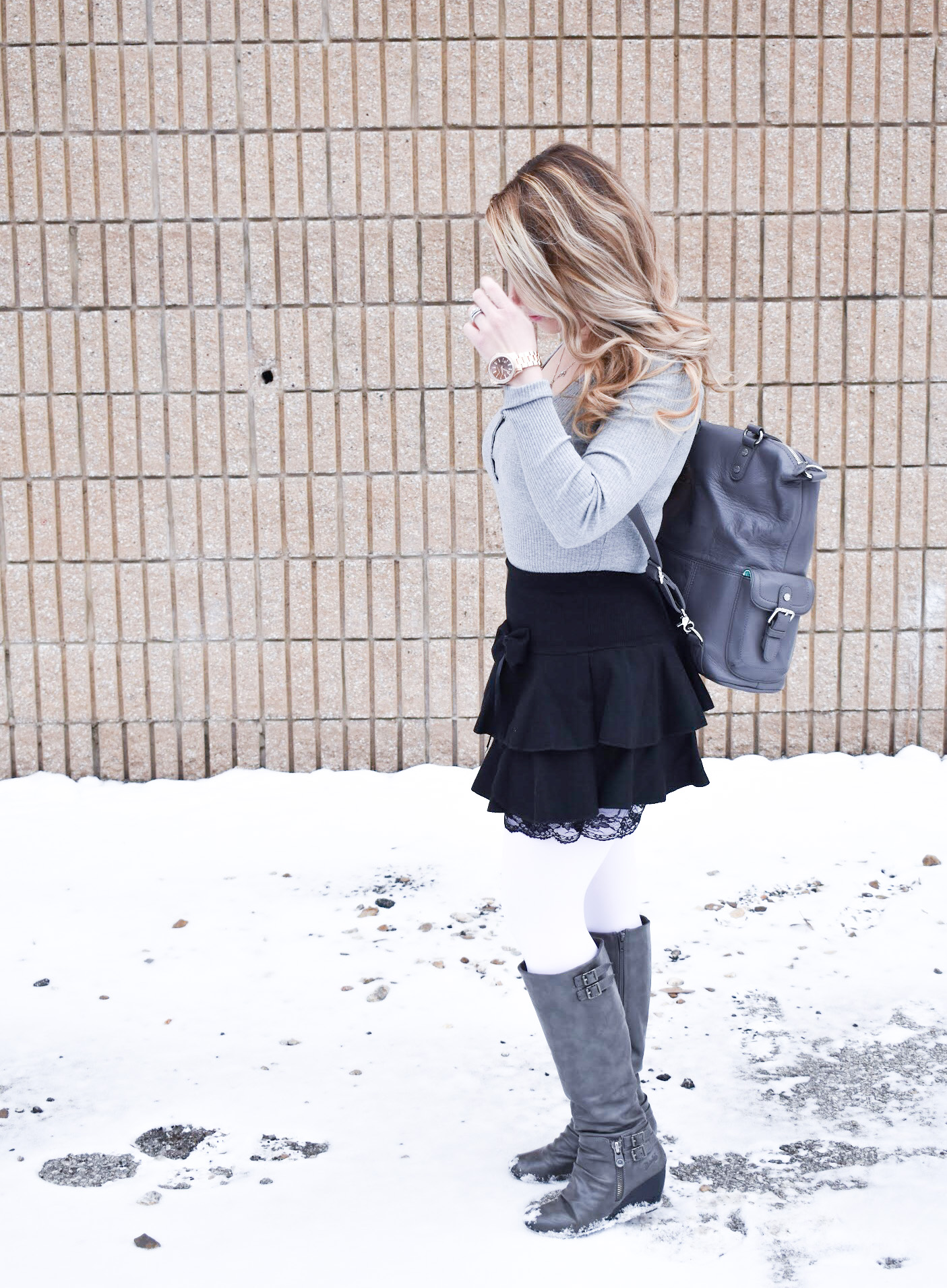 Fashion blogger COVET by tricia styles a ruffled black mini skirt with white tights, a grey bodysuit, grey wedge boots ,and a gorgeous Lily Jade diaper bag. This black mini skirt with ruffles is an affordable statement piece for your wardrobe. Check out this cute winter date night look from Kansas City fashion blogger COVET by tricia.