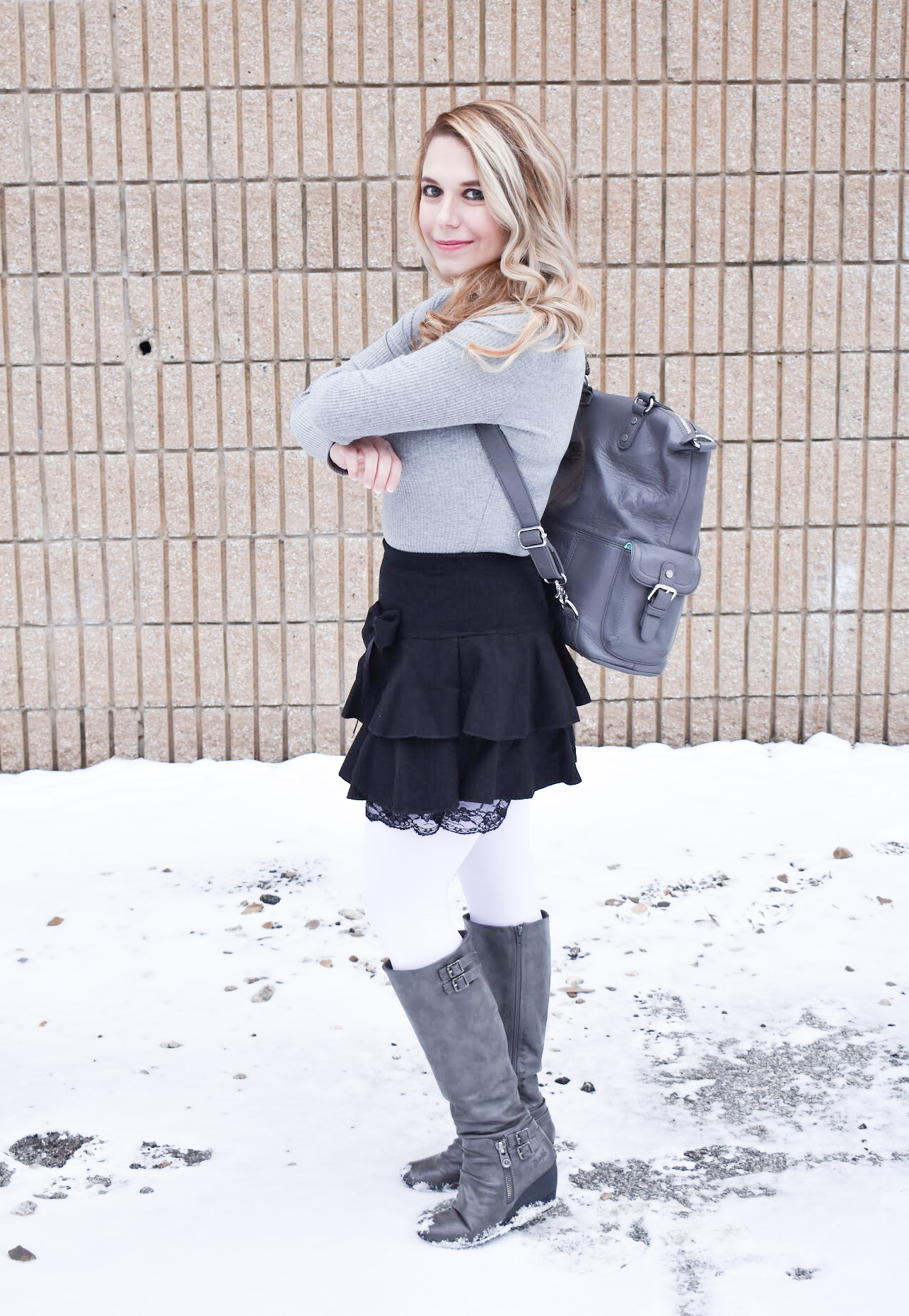 Fashion blogger COVET by tricia styles a ruffled black mini skirt with white tights, a grey bodysuit, grey wedge boots ,and a gorgeous Lily Jade diaper bag. This black mini skirt with ruffles is an affordable statement piece for your wardrobe. Check out this cute winter date night look from Kansas City fashion blogger COVET by tricia.